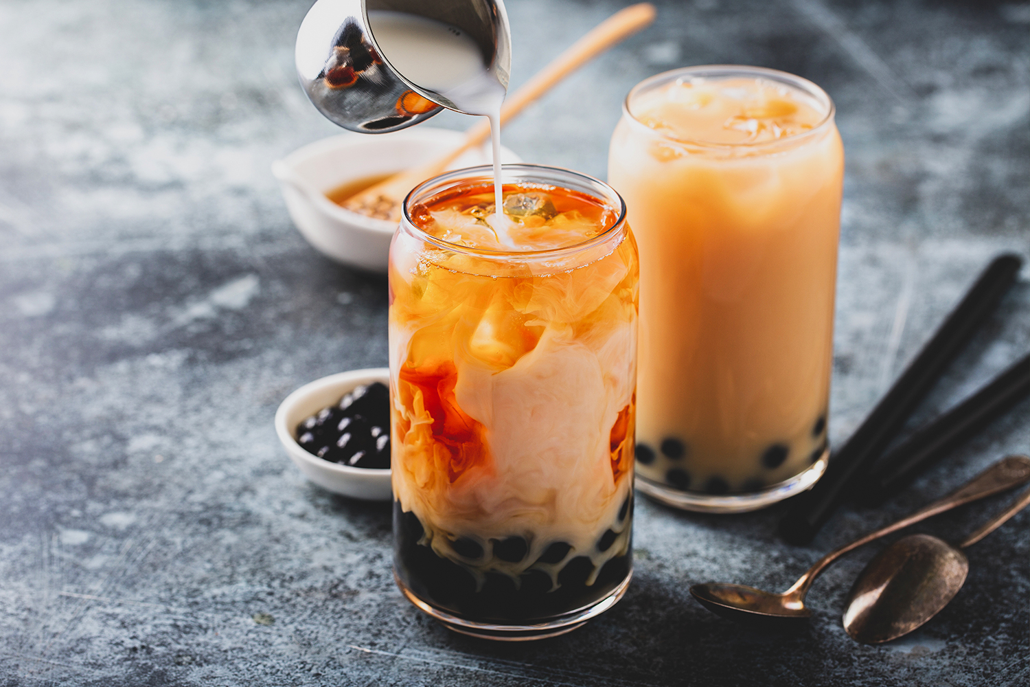 Milk tea, boba, and tapioca pearls served in a glass with more toppings on the side
