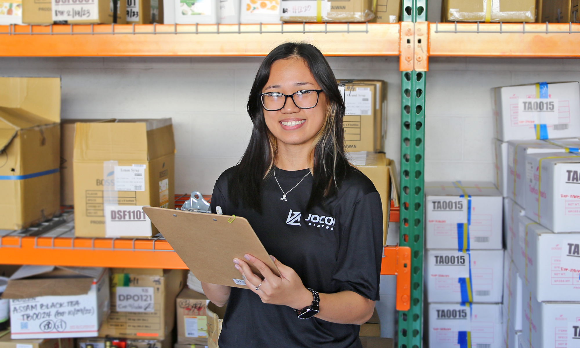 Employee smiling and holding clipboard with warehouse inventory in the background