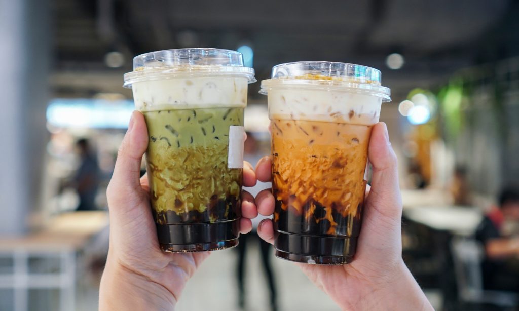 person holding a match milk tea and Thai milk tea with brown sugar walls and tapioca boba pearls